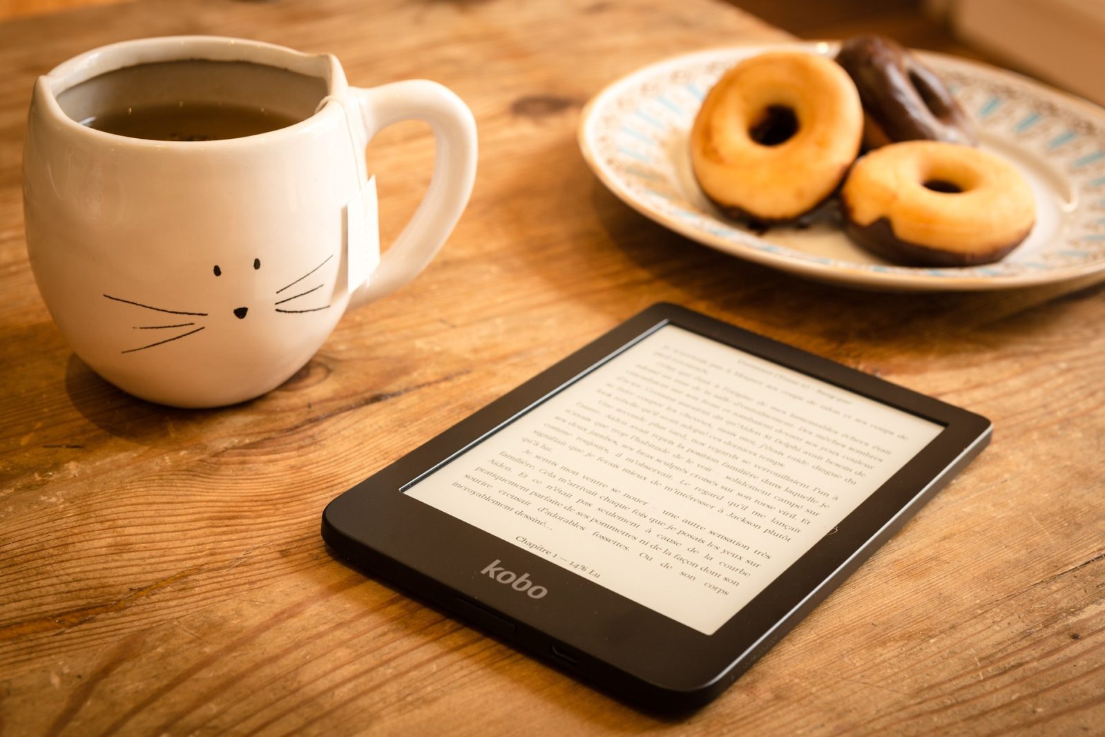Rustic table featuring a plate of mini doughnuts, a cup of coffee and a e-reader.